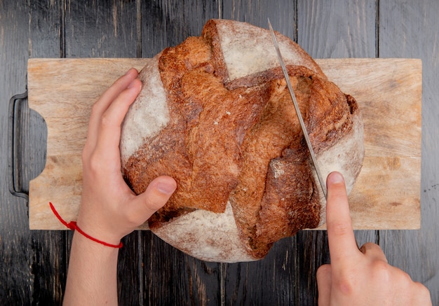 bovenaanzicht van mannelijke handen maïskolf brood met mes op snijplank op houten achtergrond te snijden