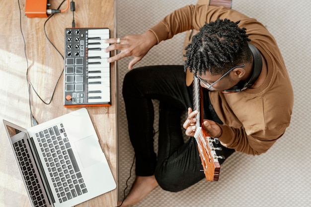 Bovenaanzicht van mannelijke muzikant thuis gitaar spelen en mengen met laptop