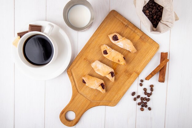 Bovenaanzicht van meelkoekjes met aardbeienjam op een houten bord met een kopje koffie op witte achtergrond