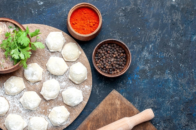 Bovenaanzicht van met bloem bestoven deegplakken met gehakt greens en paprika op donker bureau, eten rauw vlees diner gebak