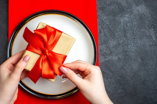 Bovenaanzicht van nationale kerstmaaltijd achtergrond met hand met lege borden met boogvormig rood lint op een rood servet op zwarte tafel