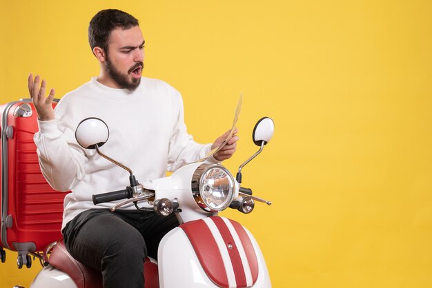 Bovenaanzicht van nerveuze jonge kerel zittend op motorfiets met koffer erop met kaart op geïsoleerde gele achtergrond