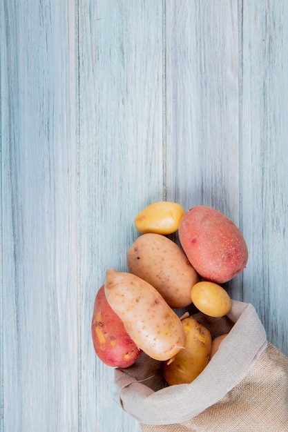 Bovenaanzicht van nieuwe roodbruine en rode aardappelen morsen uit zak op houten oppervlak met kopie ruimte