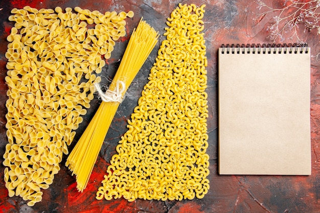 Bovenaanzicht van ongekookte pasta als een vorm van spaggetti manicotti en notebook op zwarte achtergrond