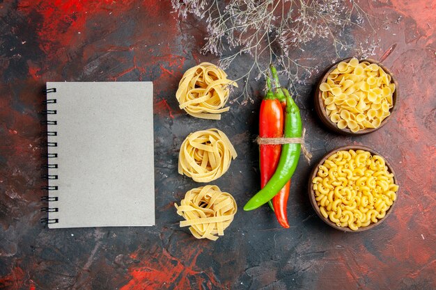 Bovenaanzicht van ongekookte pasta's cayennepeper in verschillende kleuren en maten in elkaar gebonden met touw en notitieboekje op gemengde kleur achtergrond