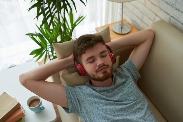 Bovenaanzicht van ontspannen student in koptelefoon genieten van zijn lounge afspeellijst