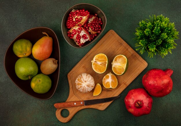 Bovenaanzicht van open en gehalveerde verse mandarijnen op een houten keukenbord met mes met open granaatappels op een kom