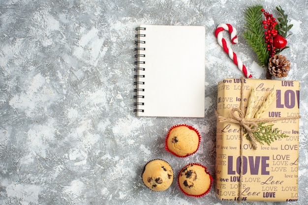 Bovenaanzicht van open notitieboekje en mooi verpakt kerstcadeau met liefdesinscriptie kleine cupcakes en sparren takken decoratie accessoires conifer kegel op ijs oppervlak