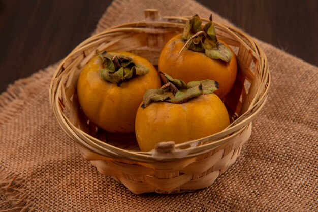 Bovenaanzicht van oranje kaki fruit op een emmer op een zakdoek op een houten tafel