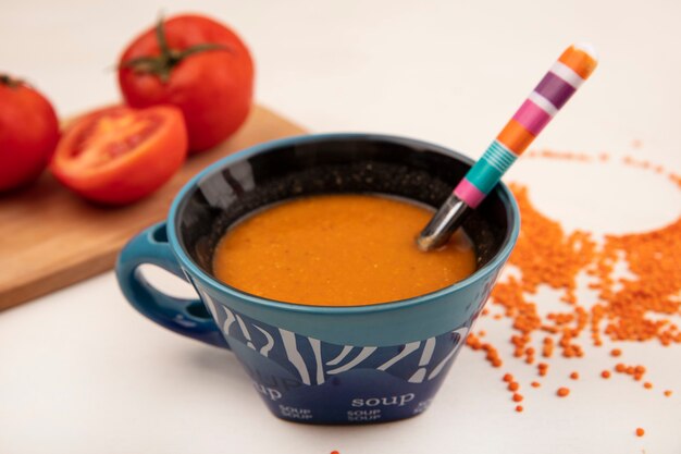 Bovenaanzicht van oranje linzensoep op een kom met lepel met tomaten op een houten keukenbord op een wit oppervlak