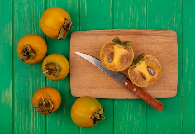 Bovenaanzicht van oranje ronde kaki vruchten op een houten keukenplank met mes op een groene houten tafel