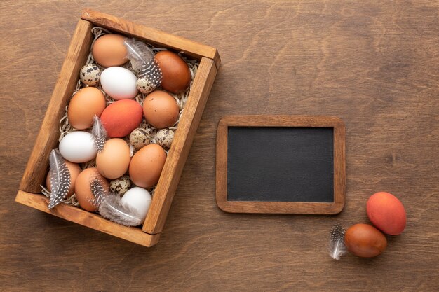 Bovenaanzicht van paaseieren in een doos met veren en schoolbord