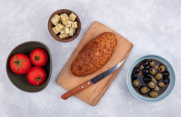 Bovenaanzicht van pasteitje op een houten keuken bord met mes met kaas tomaten en olijven op een witte achtergrond