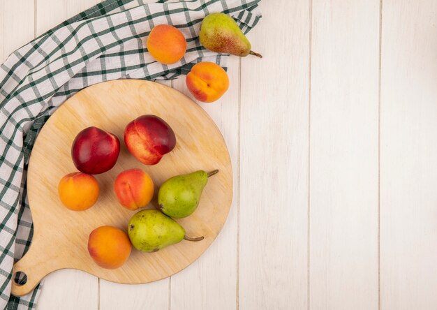 Bovenaanzicht van patroon van fruit als perzik abrikoos en peer op snijplank en op geruite doek op houten achtergrond met kopie ruimte