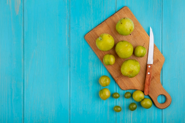 Gratis foto bovenaanzicht van patroon van fruit als plukken en pruimen met mes op snijplank en op blauwe achtergrond met kopie ruimte