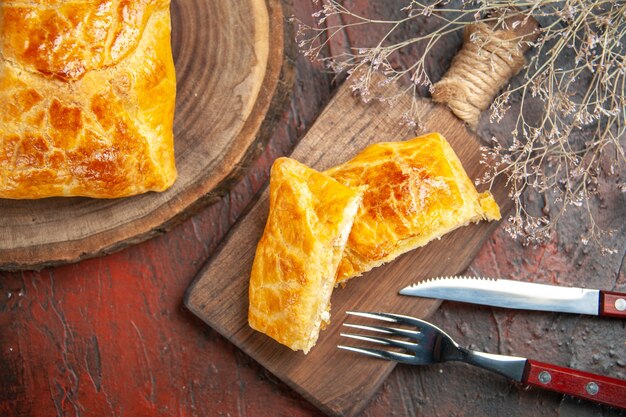 Bovenaanzicht van penovani khachapuri op houten bord en op snijplank, mes en vork op donkerrood oppervlak