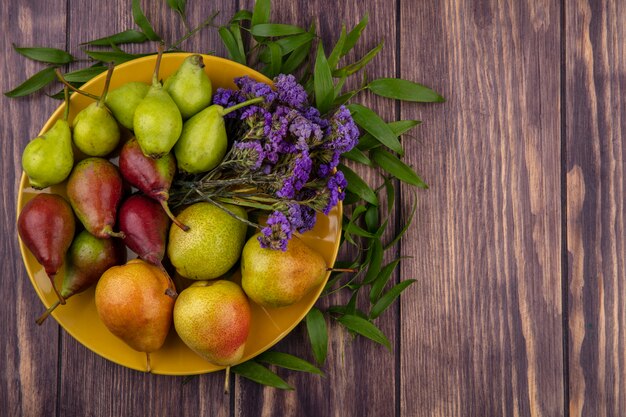 Bovenaanzicht van perziken en bloemen in plaat op houten oppervlak