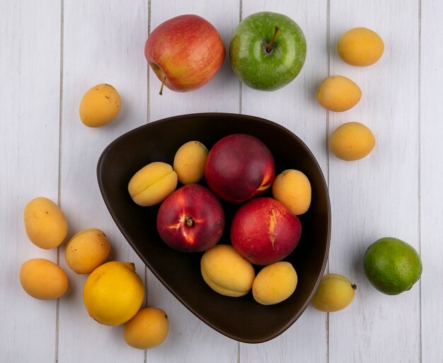 Bovenaanzicht van perziken met abrikozen in een kom met appels op een wit oppervlak