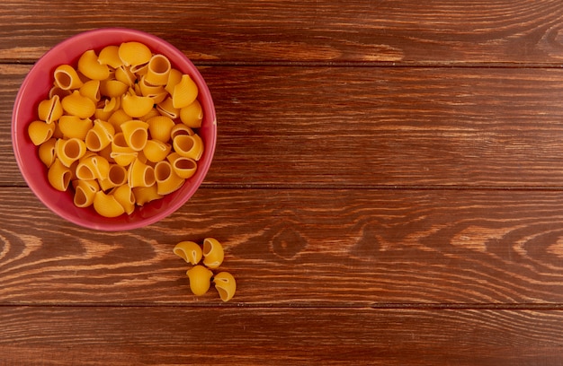 Bovenaanzicht van pijp-rigate pasta in kom op houten oppervlak met kopie ruimte