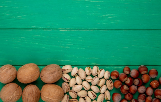 Bovenaanzicht van pistachenoten met hazelnoten en walnoten op een groene ondergrond