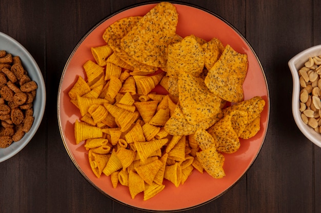 Bovenaanzicht van pittige knapperige chips op een oranje schotel met pijnboompitten op een kom op een houten tafel