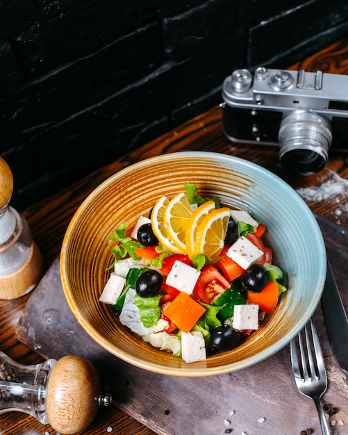 Bovenaanzicht van plantaardige salade met plakjes fetakaas en zwarte olijven in een kom op een houten tafel
