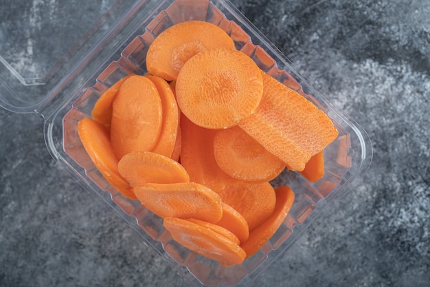 Bovenaanzicht van plastic container vol met plakjes wortel over grijze achtergrond.