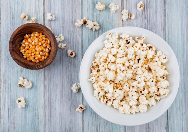 Bovenaanzicht van popcorn op een witte plaat met likdoorns op een houten kom op grijze ondergrond