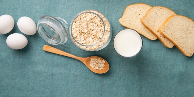 Bovenaanzicht van pot vol havervlokken met eieren melk witbrood plakjes en houten lepel op blauwe achtergrond met kopie ruimte