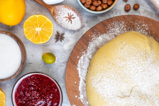 Bovenaanzicht van rauw gebakmeel op een ronde houten lepel, havermout, vers fruit, jamsuiker op een gebeitste witte achtergrond