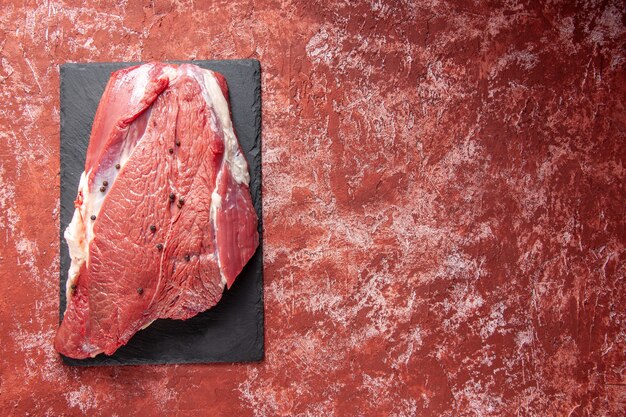 Bovenaanzicht van rauw vers rood vlees op zwart bord aan de rechterkant op oliepastelrode achtergrond met vrije ruimte