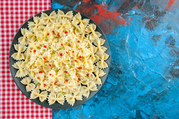 Bovenaanzicht van rauwe italiaanse farfalle pasta met groenten op rode gestripte handdoek op blauwe tafel