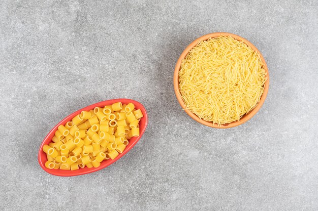 Bovenaanzicht van rauwe pasta en vermicelli op grijze tafel.