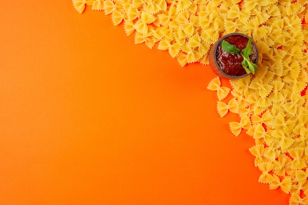 Bovenaanzicht van rauwe pasta farfalle met ketchup in een pan en kopieer de ruimte op oranje