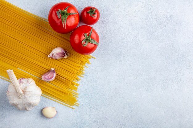 Bovenaanzicht van rauwe spaghetti met knoflook en tomaten op een grijze ondergrond