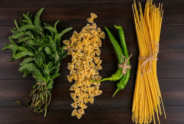 Bovenaanzicht van rauwe spaghetti met pasta chili peper en een bosje munt op een houten oppervlak