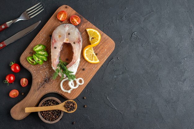 Bovenaanzicht van rauwe vis en vers gehakte groenten plakjes citroen specerijen op een houten bord bestek aan de rechterkant op zwarte verontruste oppervlak