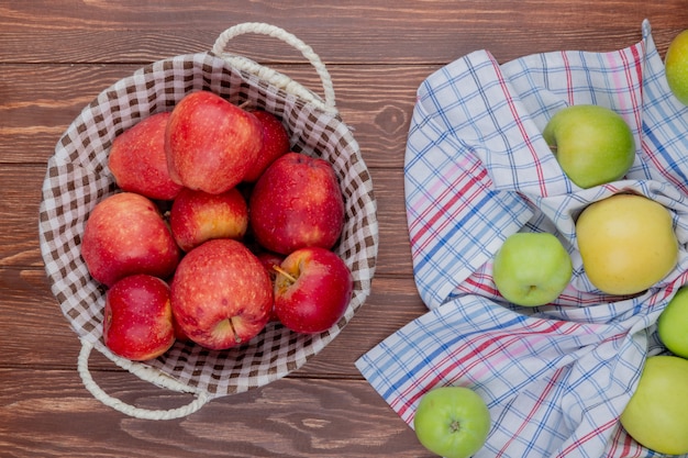 Bovenaanzicht van rode appels in mand met groene op geruite doek op houten achtergrond