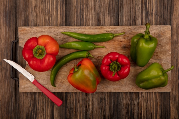 Bovenaanzicht van rode en groene paprika's op een houten keukenbord met mes op een houten oppervlak