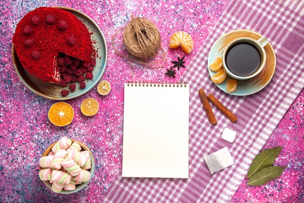 Bovenaanzicht van rode frambozencake met kaneelmandarijnen en thee op het roze oppervlak