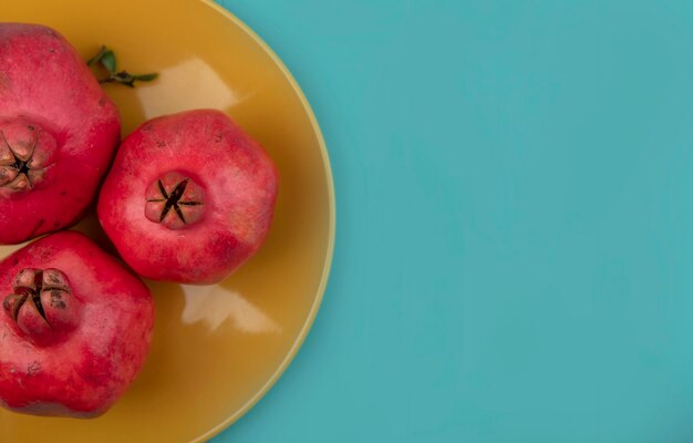 Bovenaanzicht van rode verse granaatappels op een gele plaat op een blauwe achtergrond met kopie ruimte