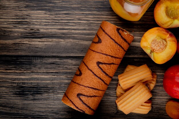 bovenaanzicht van roll cake met koekjes en perzik jam in een glazen pot op rustieke houten tafel met kopie ruimte