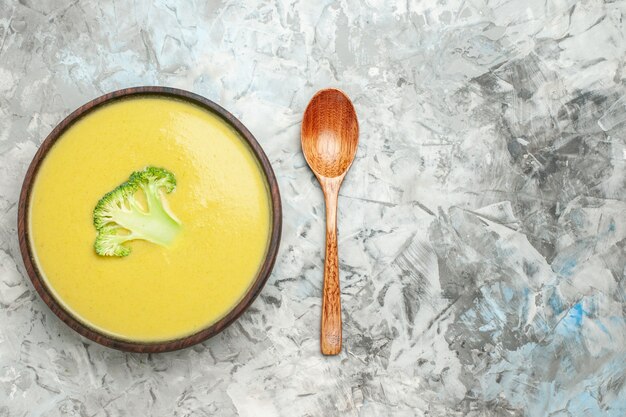 Bovenaanzicht van romige broccolisoep in een bruine kom en lepel op grijze lijst