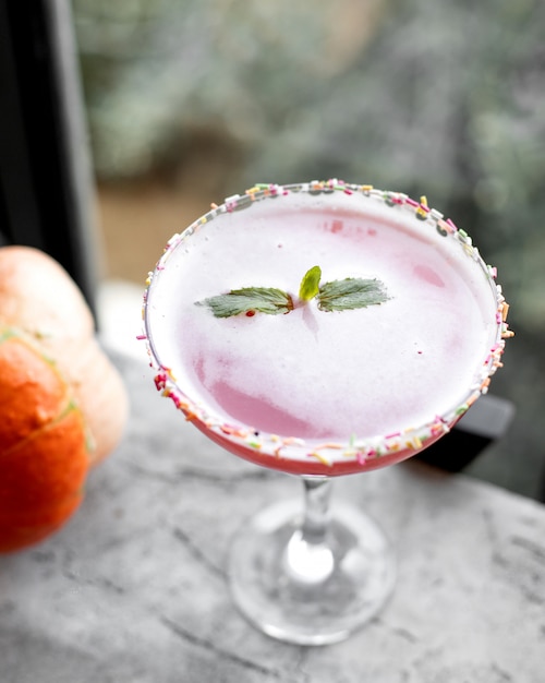 Bovenaanzicht van roze cocktail in lange steel glas gegarneerd met kokos hagelslag