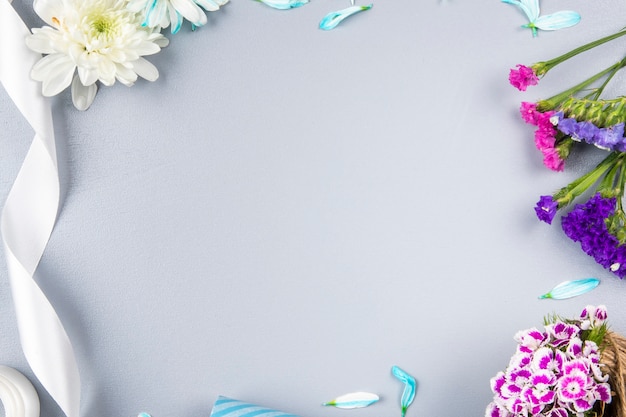 Bovenaanzicht van roze en paarse statice bloemen met witte chrysant en lint op witte tafel met kopie ruimte