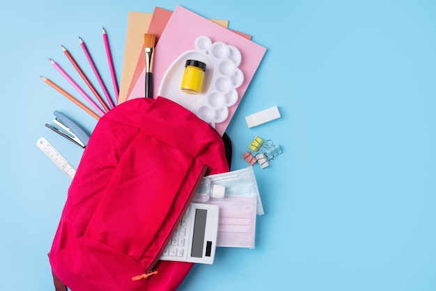 Bovenaanzicht van roze rugzak met school briefpapier over blauwe tafel achtergrond, terug naar school ontwerpconcept.