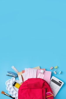 Bovenaanzicht van roze rugzak met school briefpapier over blauwe tafel achtergrond, terug naar school ontwerpconcept. Premium Foto