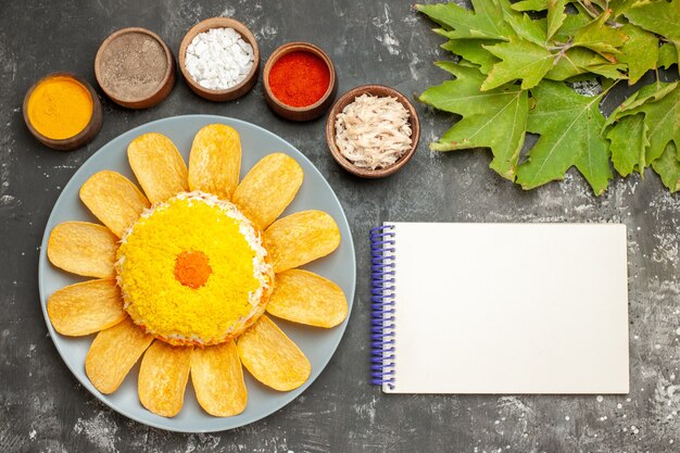 Bovenaanzicht van salade aan de linkerkant met kruiden en notitieblok aan de zijkant met bladeren aan de rechterkant op donkergrijze tafel