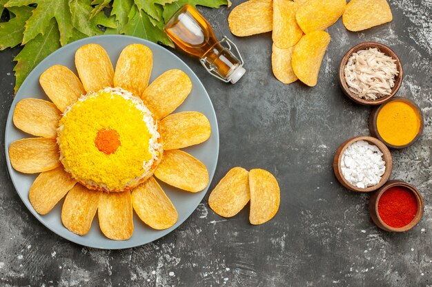 Bovenaanzicht van salade met krokante frietjes van de oliefles en bladeren aan de kant met kruiden ernaast op donkergrijze tafel