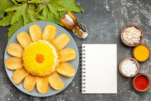 Bovenaanzicht van salade met oliefles Kladblok en bladeren aan de zijkant met kruiden ernaast op donkergrijze tafel